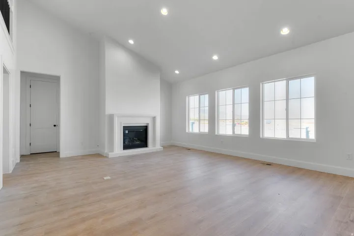 Unfurnished living room with lofted ceiling, light wood finished floors, recessed lighting, and a glass covered fireplace