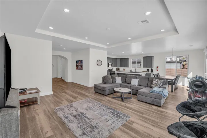 Living room featuring a tray ceiling, light wood-style floors, arched walkways, and a chandelier