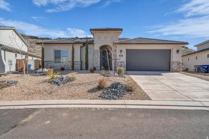 View of front of home with stone siding, an attached garage, stucco siding, driveway, and a tiled roof