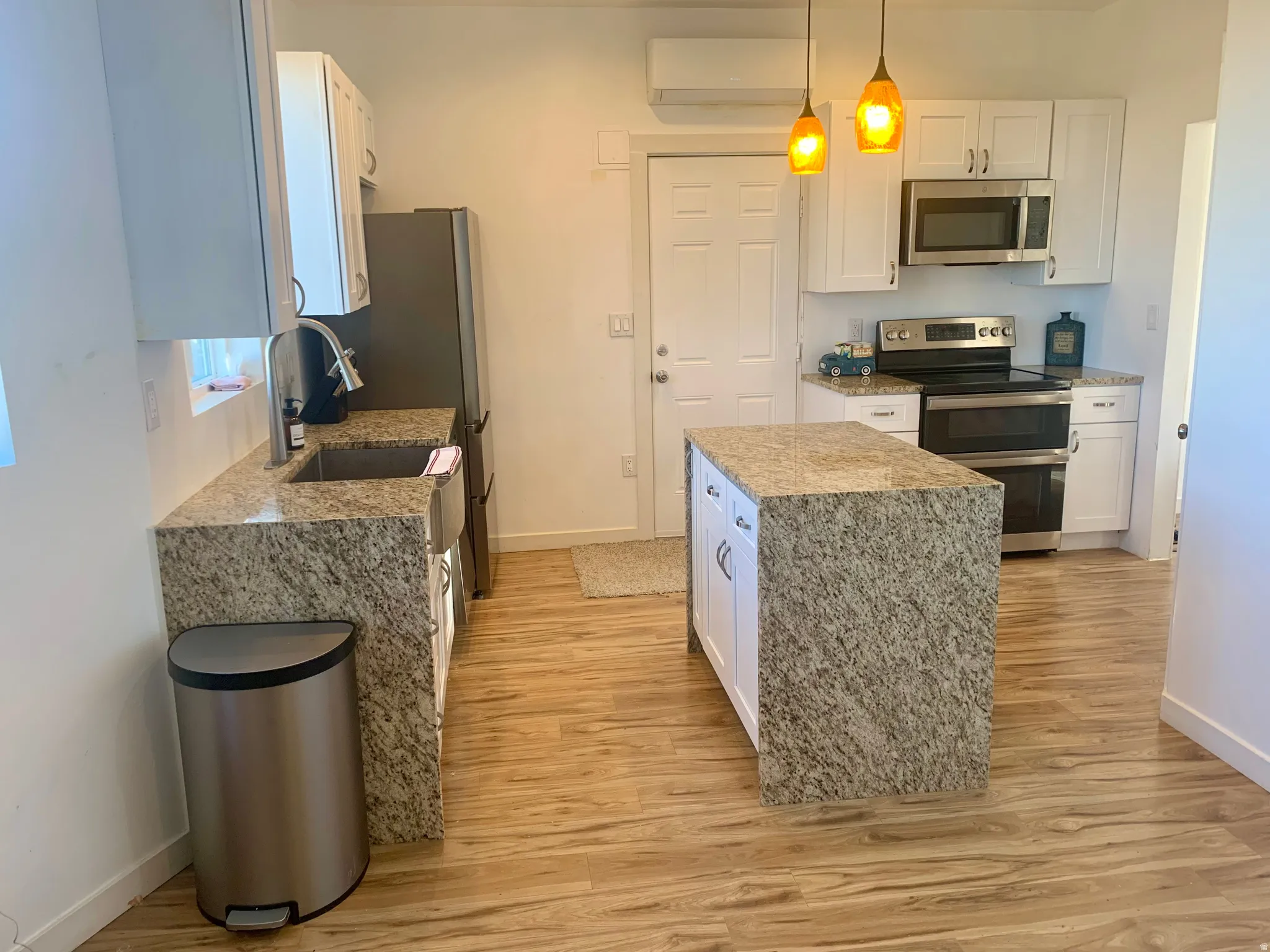 Kitchen with white cabinets, light stone countertops, stainless steel appliances, and light wood finished floors