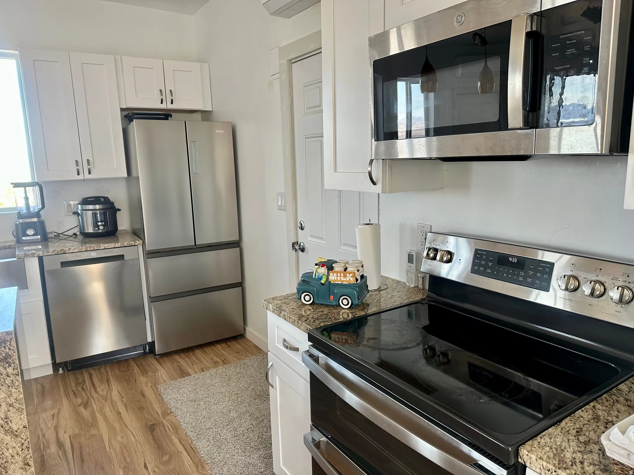 Kitchen featuring stainless steel appliances, white cabinets, light wood-style flooring, and dark stone counters