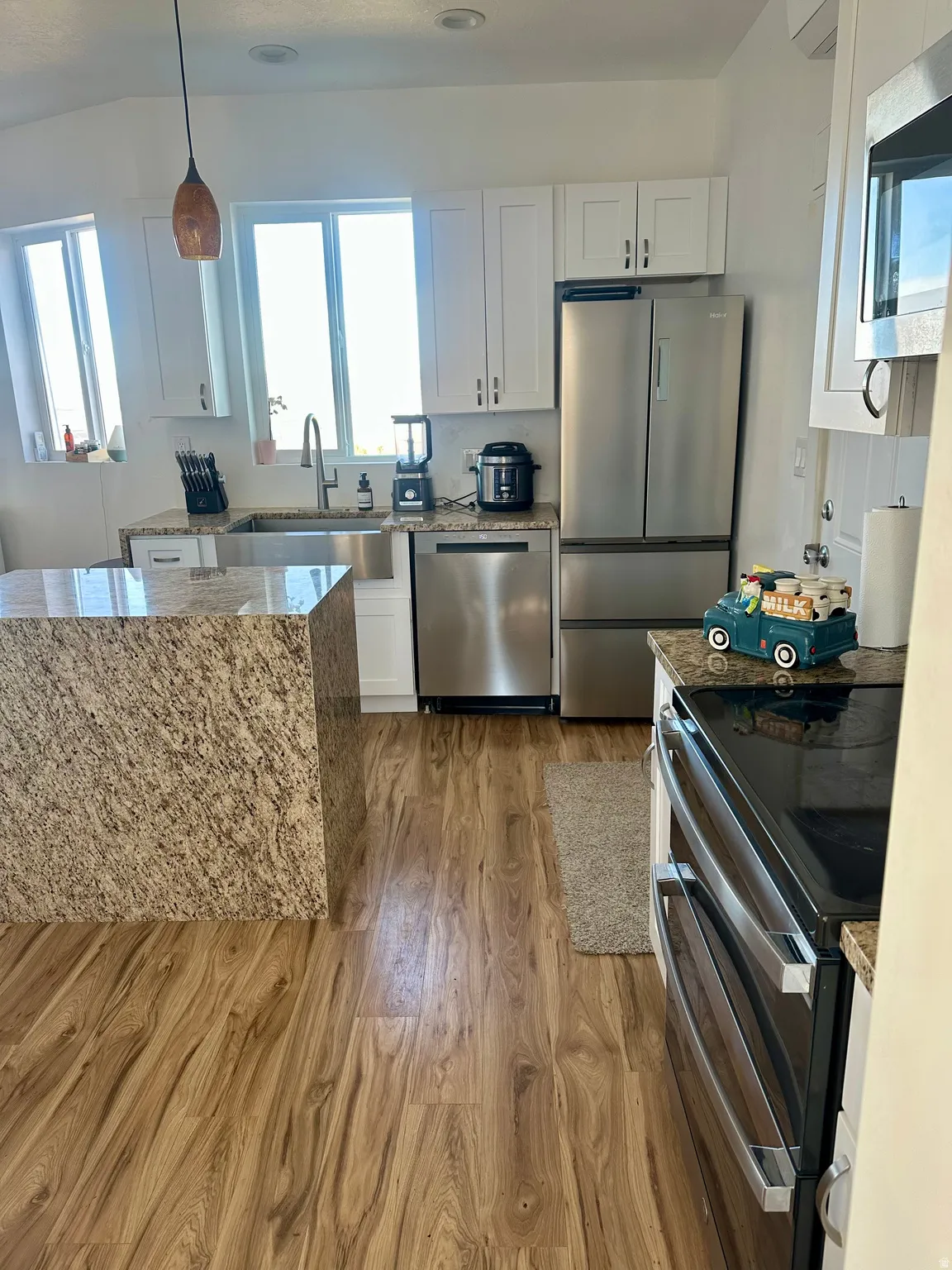 Kitchen featuring stainless steel appliances, white cabinetry, light wood finished floors, light stone countertops, and hanging light fixtures