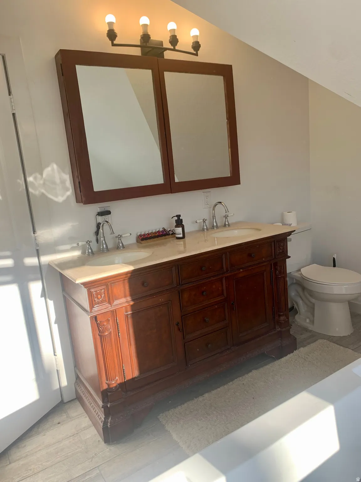 Bathroom featuring double vanity, light wood-style floors, and vaulted ceiling