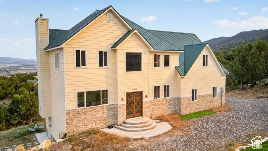 Two-story residential building featuring light-colored siding, a dark green metal roof, and stone veneer accents