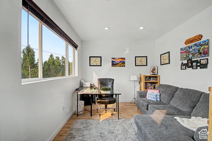 Bright interior space featuring a wide window with outdoor tree scenery, recessed ceiling lighting, and wood-finish flooring