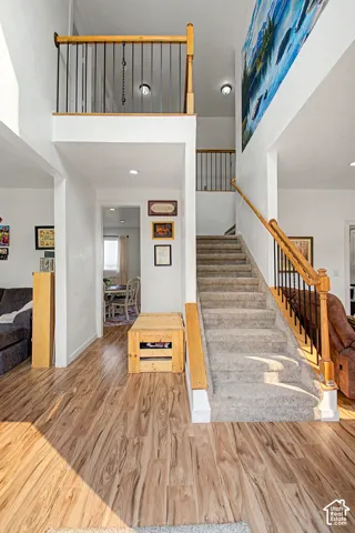 Grand entryway featuring wood-finish flooring, a carpeted staircase with wood handrails and black balusters, and a high-ceiling open landing