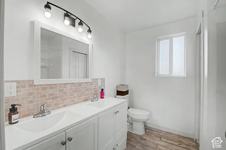 Bathroom featuring a double vanity with integrated sinks, brick-patterned tile backsplash, a wall-mounted mirror, and a window providing illumination