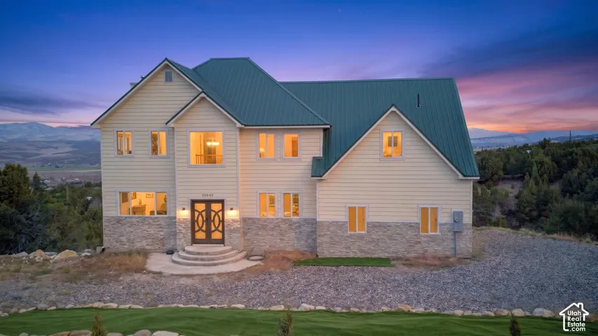 Multi-story property featuring a prominent metal roof, light-toned siding, and stone accents