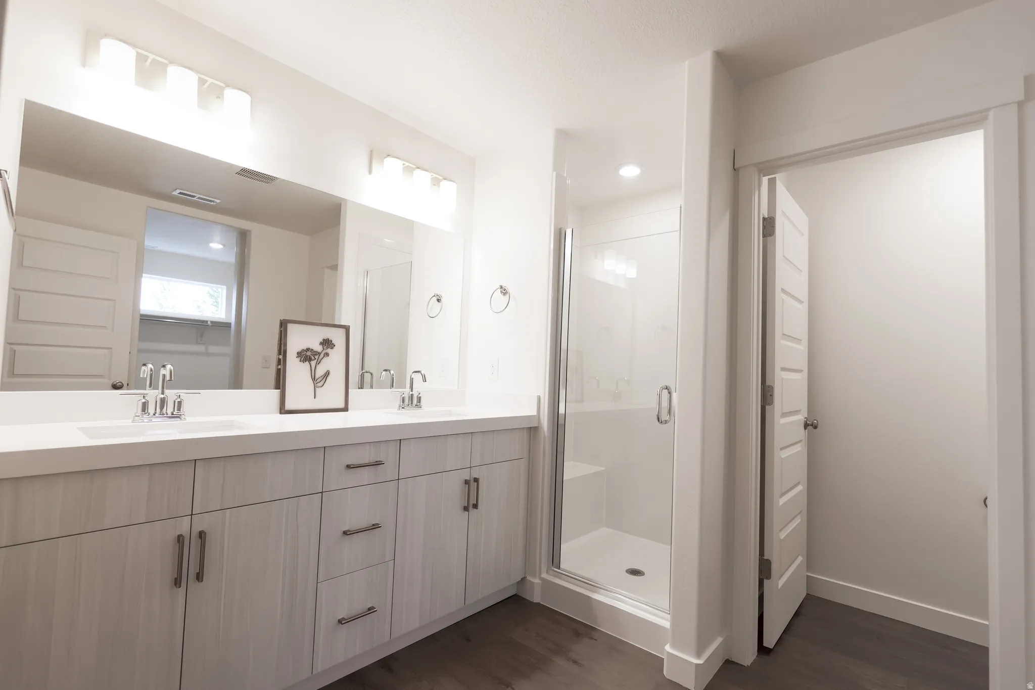 Bathroom featuring double vanity, a shower stall, and dark wood-style floors