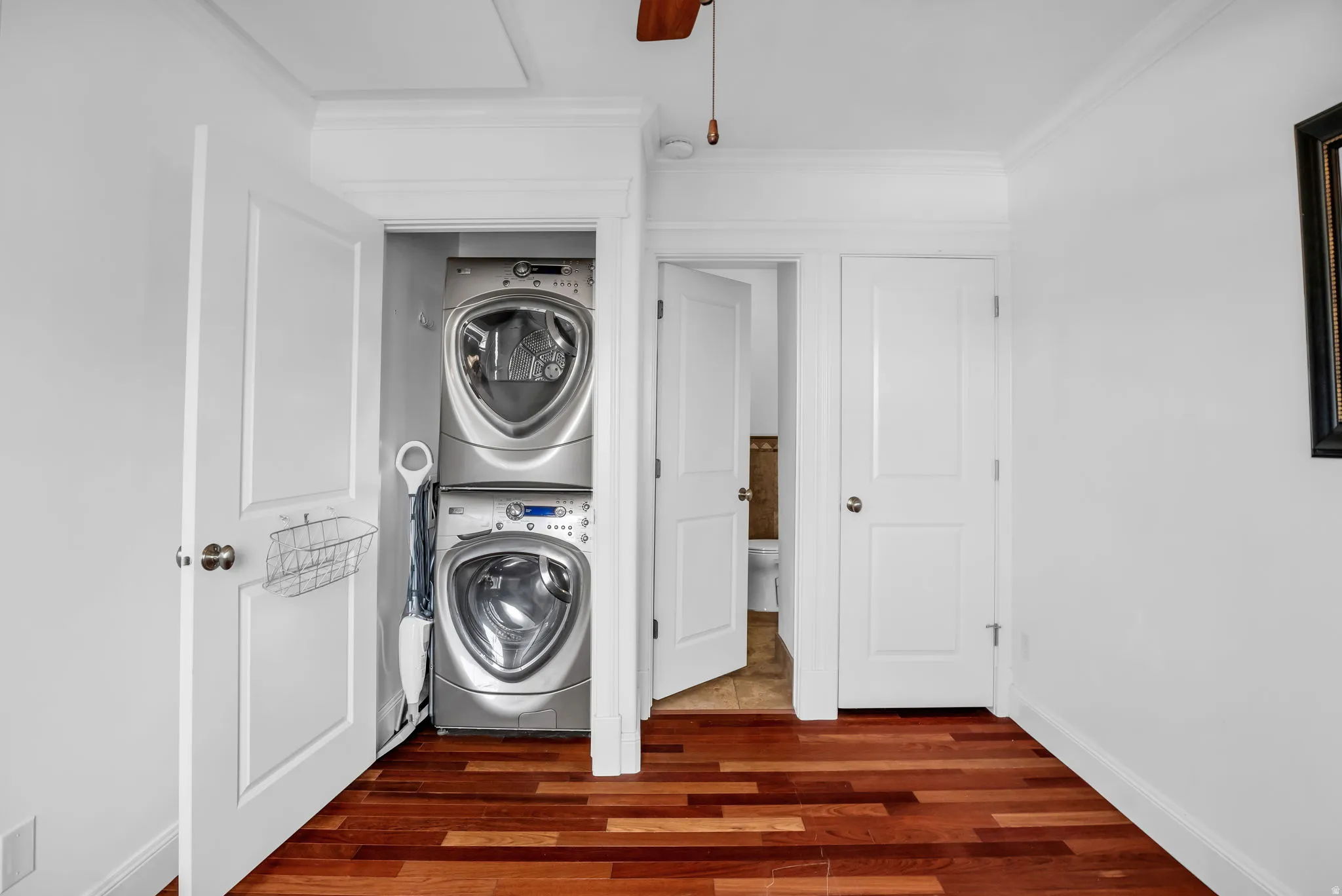 Laundry area featuring dark wood finished floors, ornamental molding, stacked washer and dryer, and ceiling fan