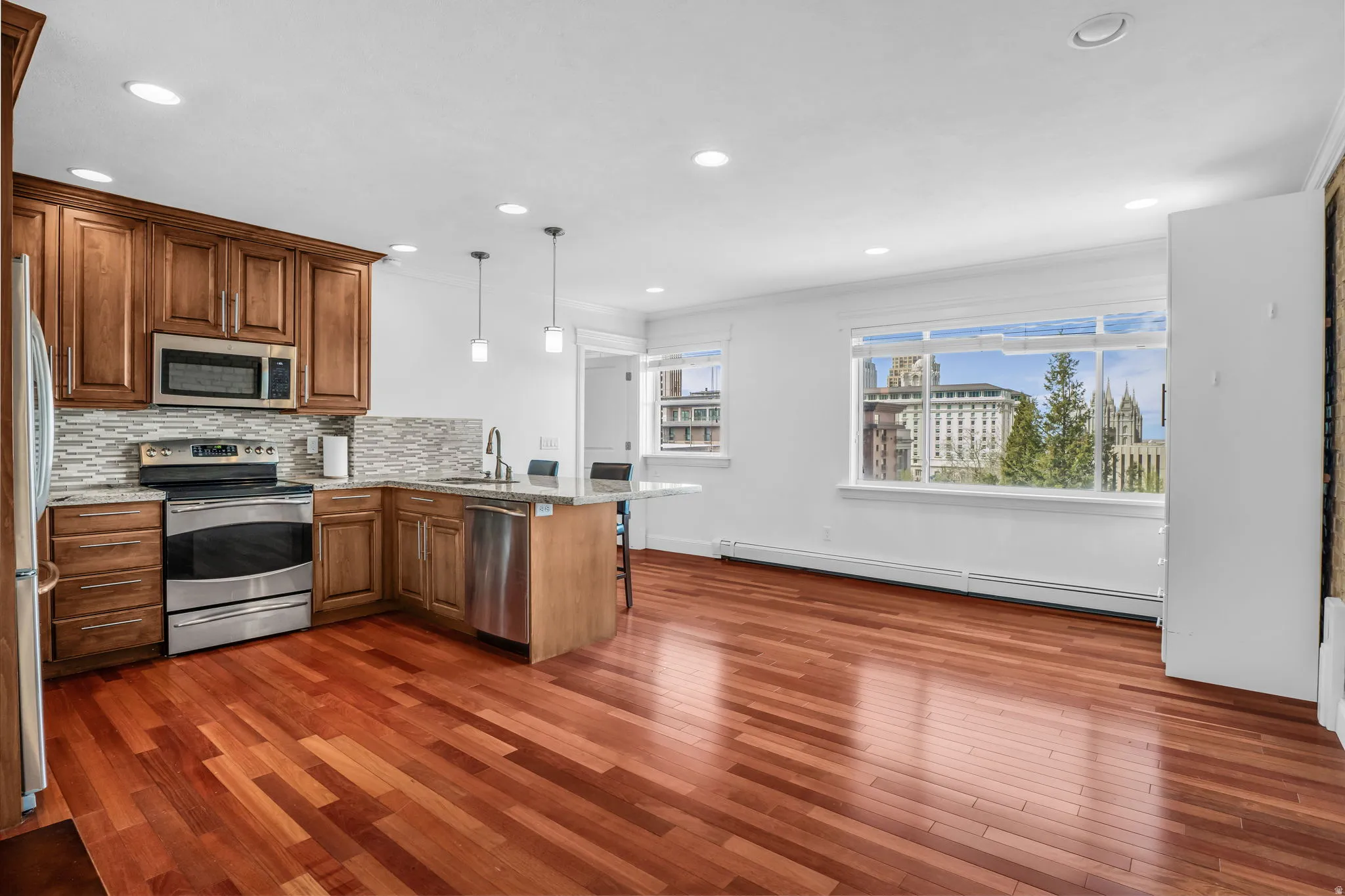 Kitchen featuring a peninsula, stainless steel appliances, baseboard heating, wood finish cabinetry, and a kitchen breakfast bar