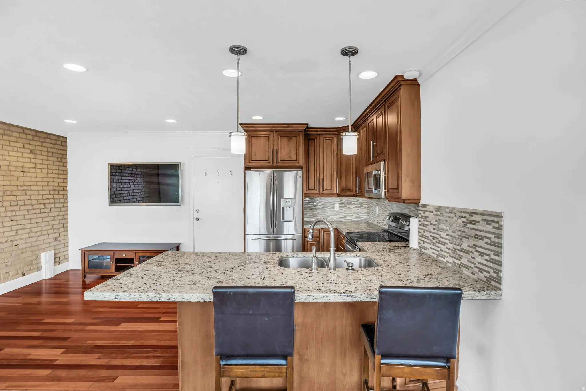 Kitchen featuring wood finish cabinetry, a peninsula, ornamental molding, light stone countertops, and a breakfast bar area