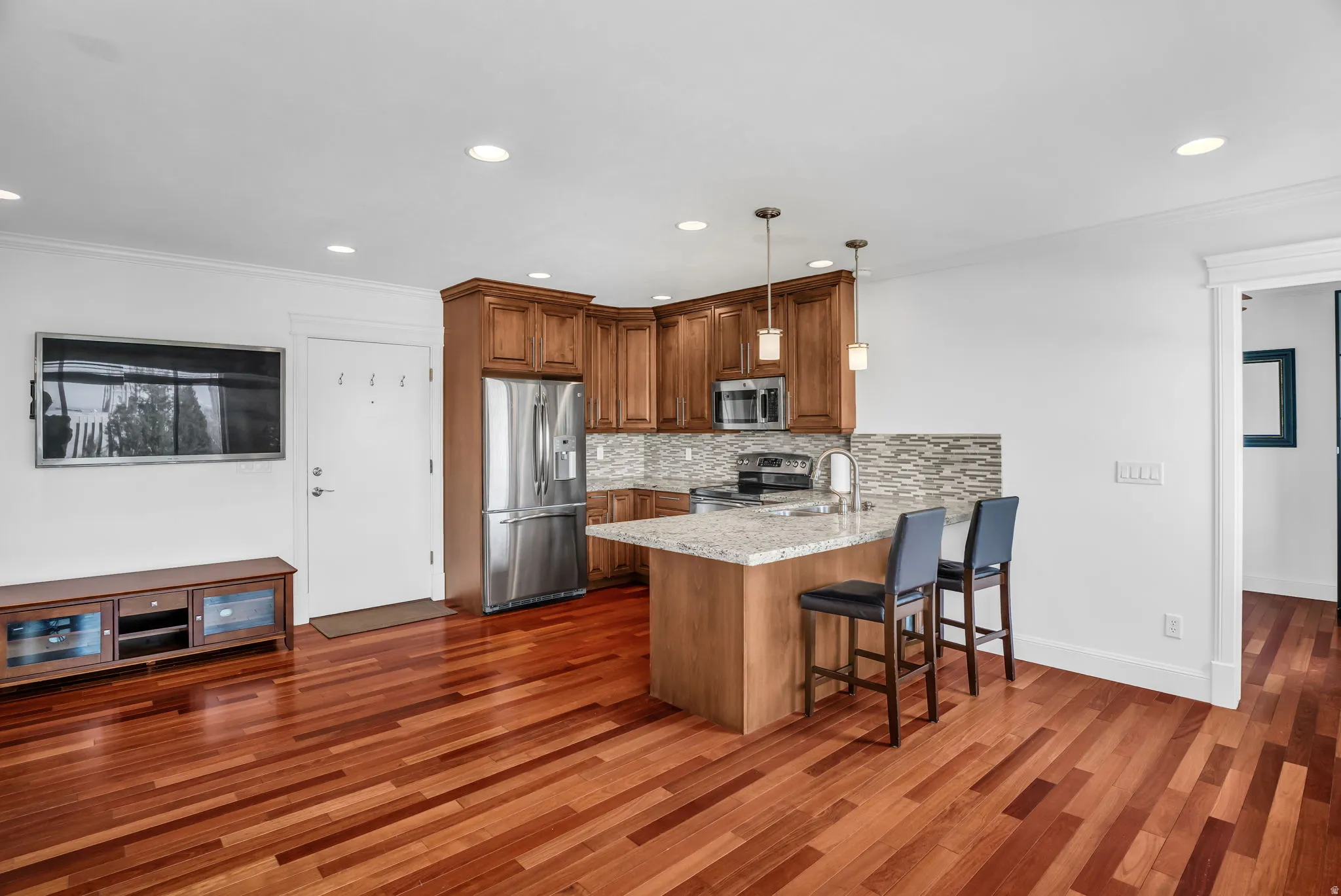 Kitchen with wood finish cabinetry, stainless steel appliances, a peninsula, a breakfast bar, and pendant lighting