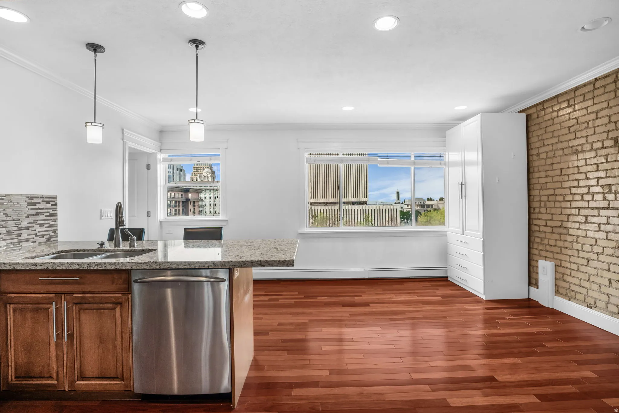 Kitchen with stainless steel dishwasher, ornamental molding, brick wall, dark wood finished floors, and a peninsula