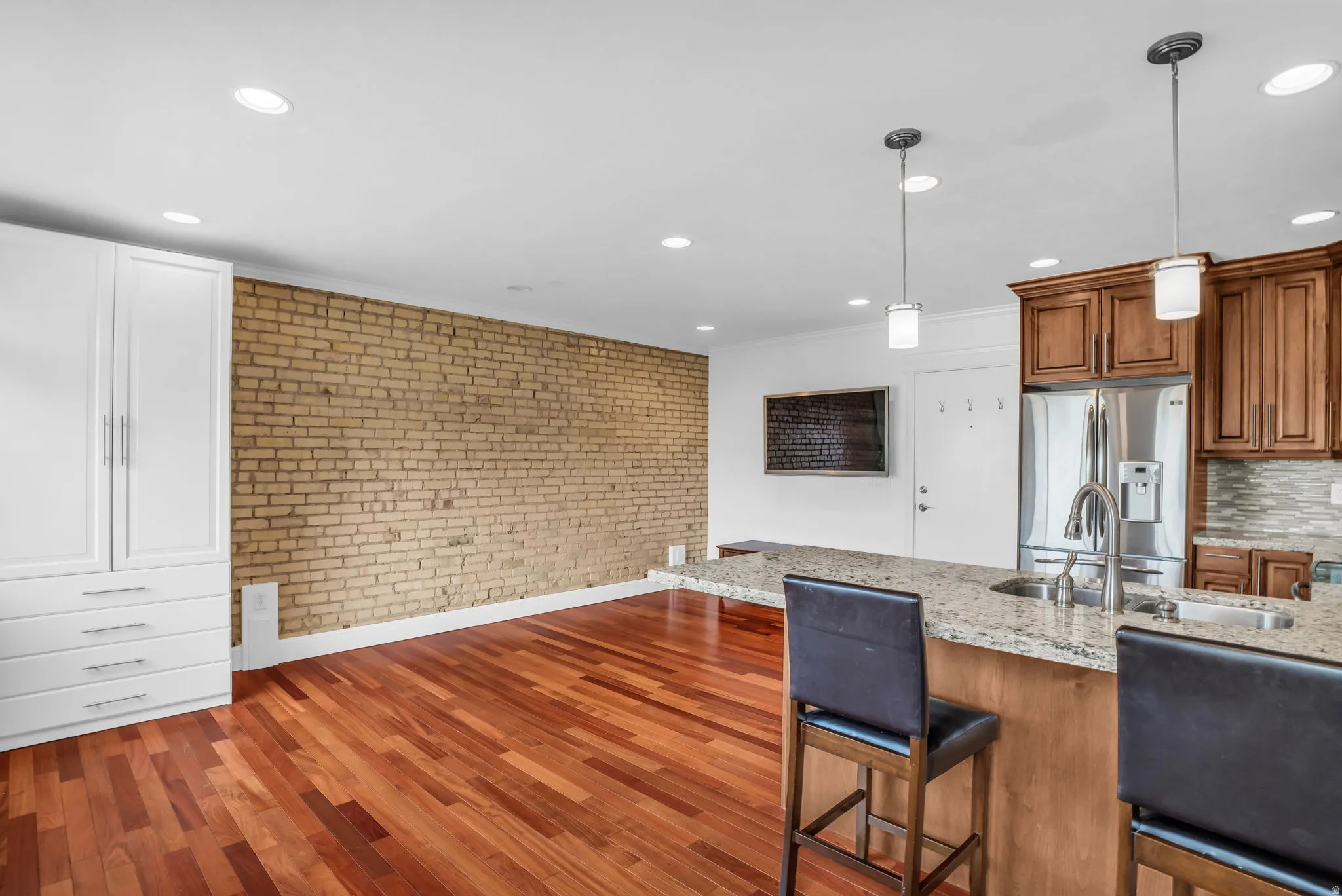 Kitchen with brick wall, light stone countertops, wood finish cabinetry, a kitchen bar, and stainless steel fridge with ice dispenser