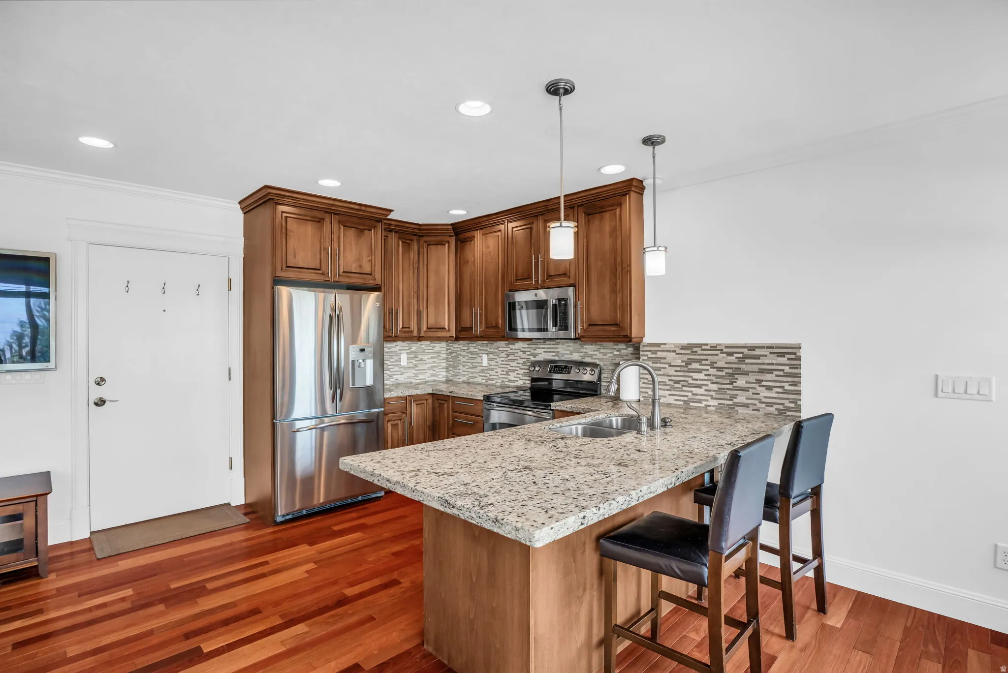 Kitchen featuring stainless steel appliances, ornamental molding, light stone counters, wood finish cabinetry, and a peninsula