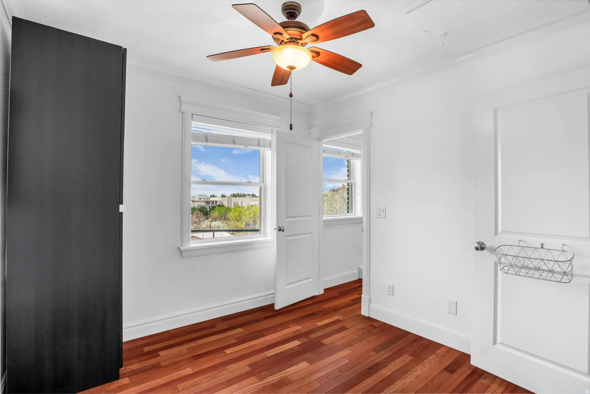 Unfurnished bedroom featuring dark wood-style floors, ceiling fan, and ornamental molding