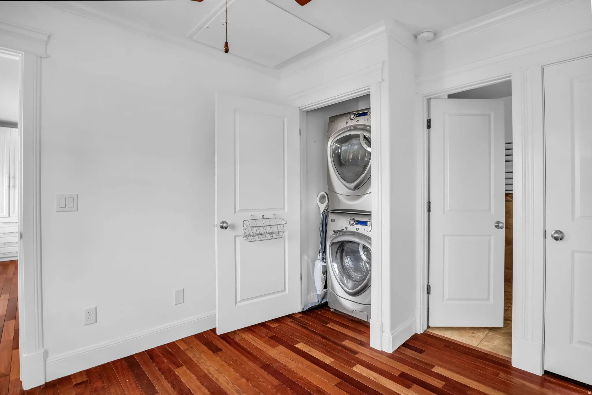 Laundry area featuring stacked washer / dryer, wood-type flooring, ornamental molding, and ceiling fan