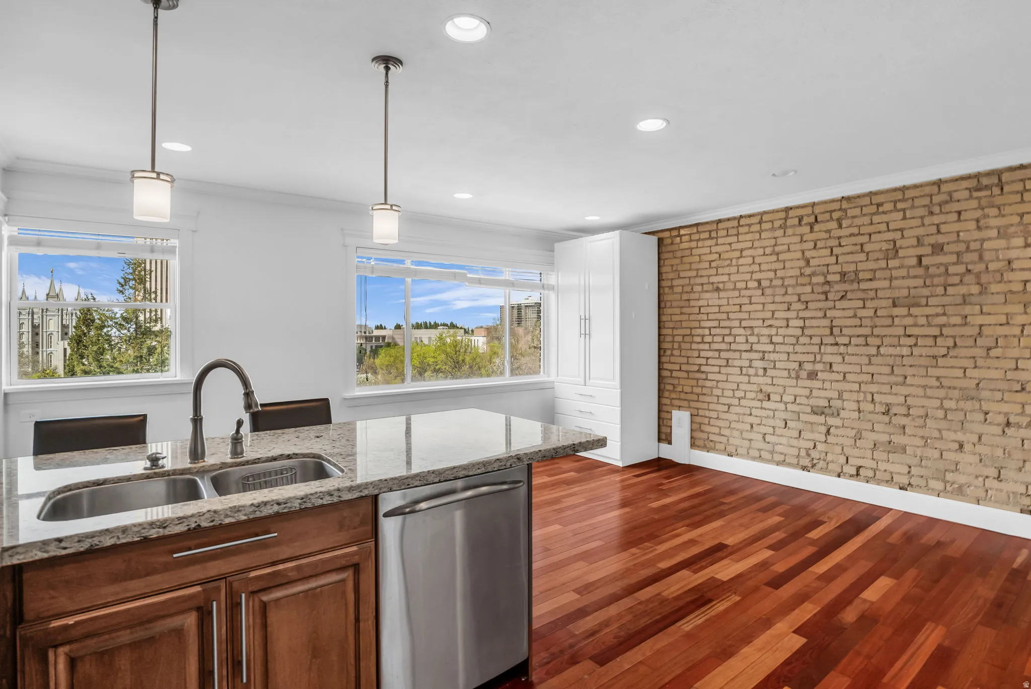 Kitchen featuring brick wall, dishwasher, light stone countertops, ornamental molding, and wood finish cabinetry