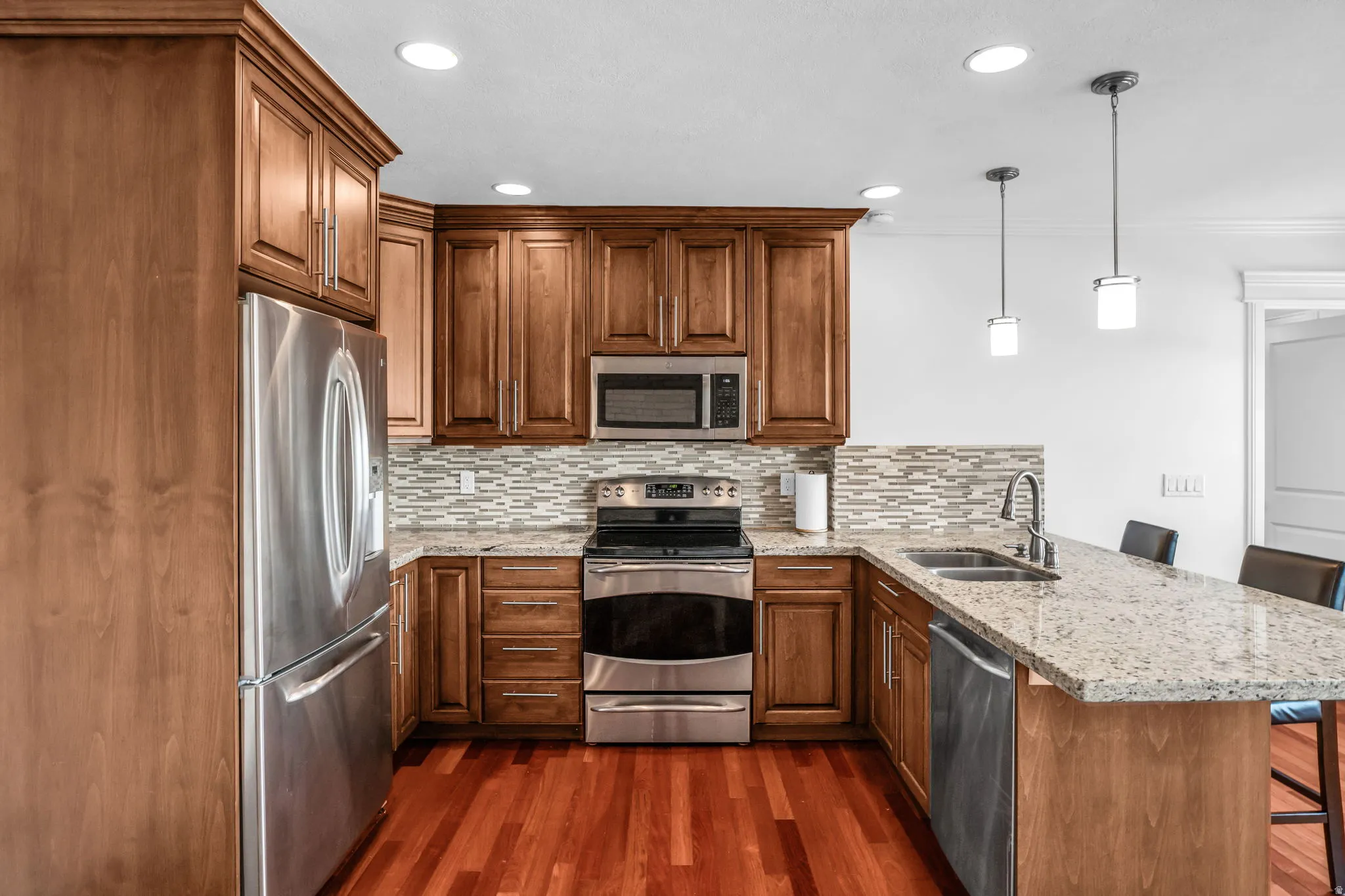 Kitchen with a peninsula, a breakfast bar area, light stone counters, stainless steel appliances, and hanging light fixtures