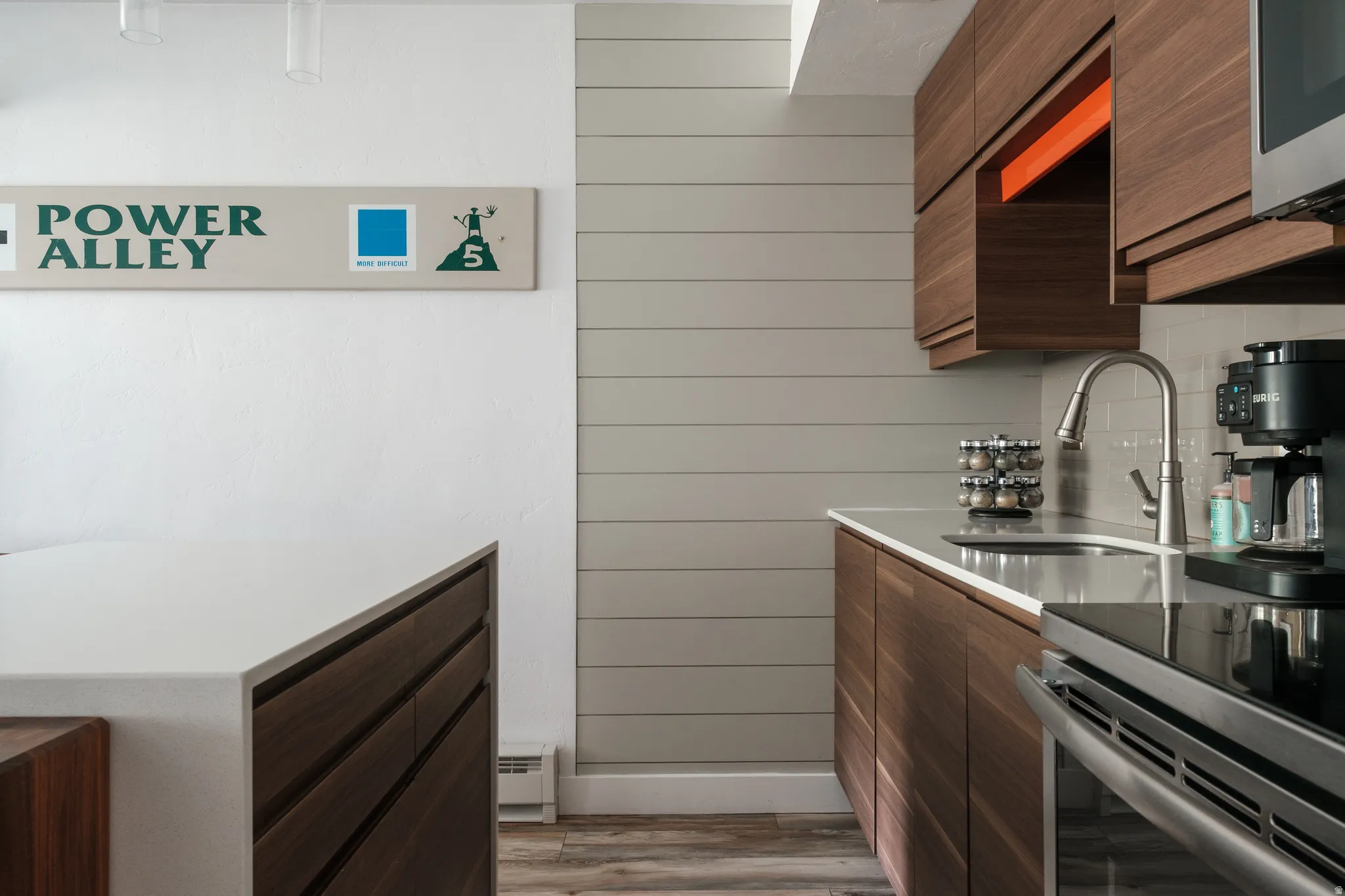 Kitchen with modern cabinets, dark wood finish cabinetry, wooden walls, stainless steel appliances, and baseboard heating