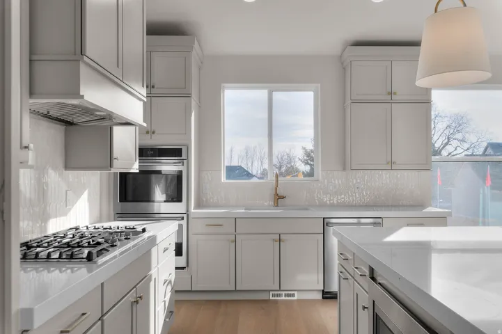 Kitchen featuring stainless steel appliances, light wood finished floors, light stone counters, and hanging light fixtures