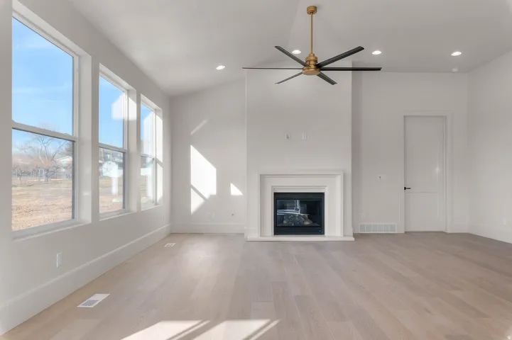 Unfurnished living room featuring a ceiling fan, light wood finished floors, a glass covered fireplace, recessed lighting, and vaulted ceiling