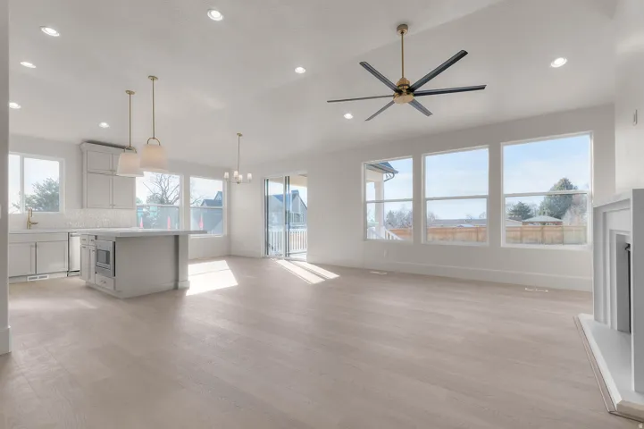 Unfurnished living room featuring light wood-style floors, a ceiling fan, a fireplace with raised hearth, suspended lighting, and vaulted ceiling