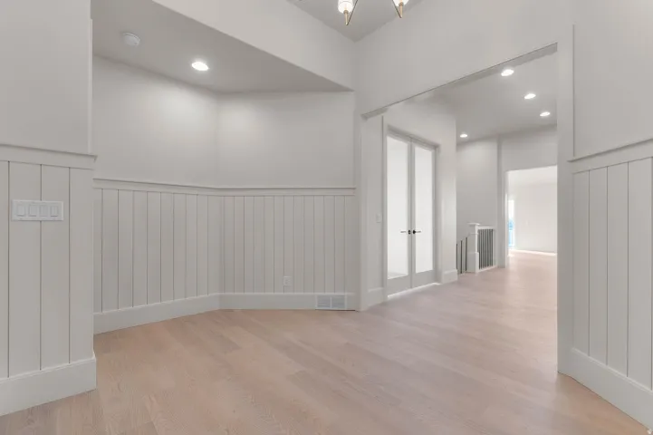Corridor with a wainscoted wall, light wood-style flooring, and a chandelier