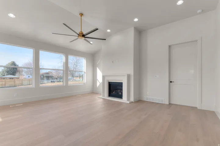 Unfurnished living room with a ceiling fan, lofted ceiling, light wood-style flooring, a glass covered fireplace, and recessed lighting