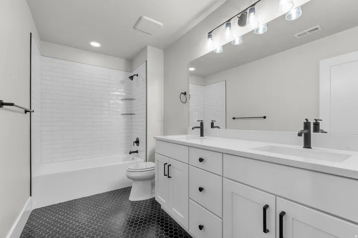 Bathroom featuring double vanity, dark tile patterned flooring, and shower / washtub combination