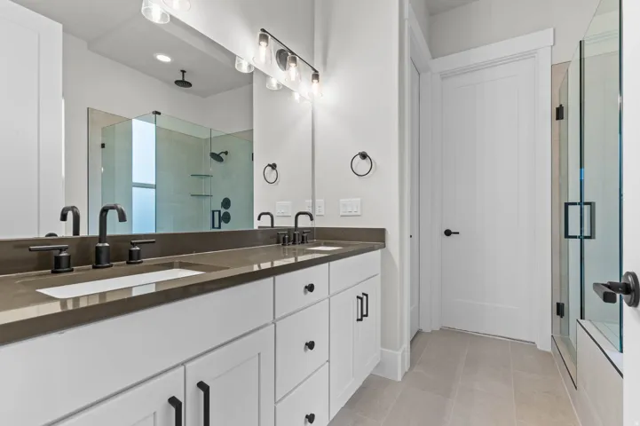 Bathroom with a shower stall, double vanity, and light tile patterned flooring
