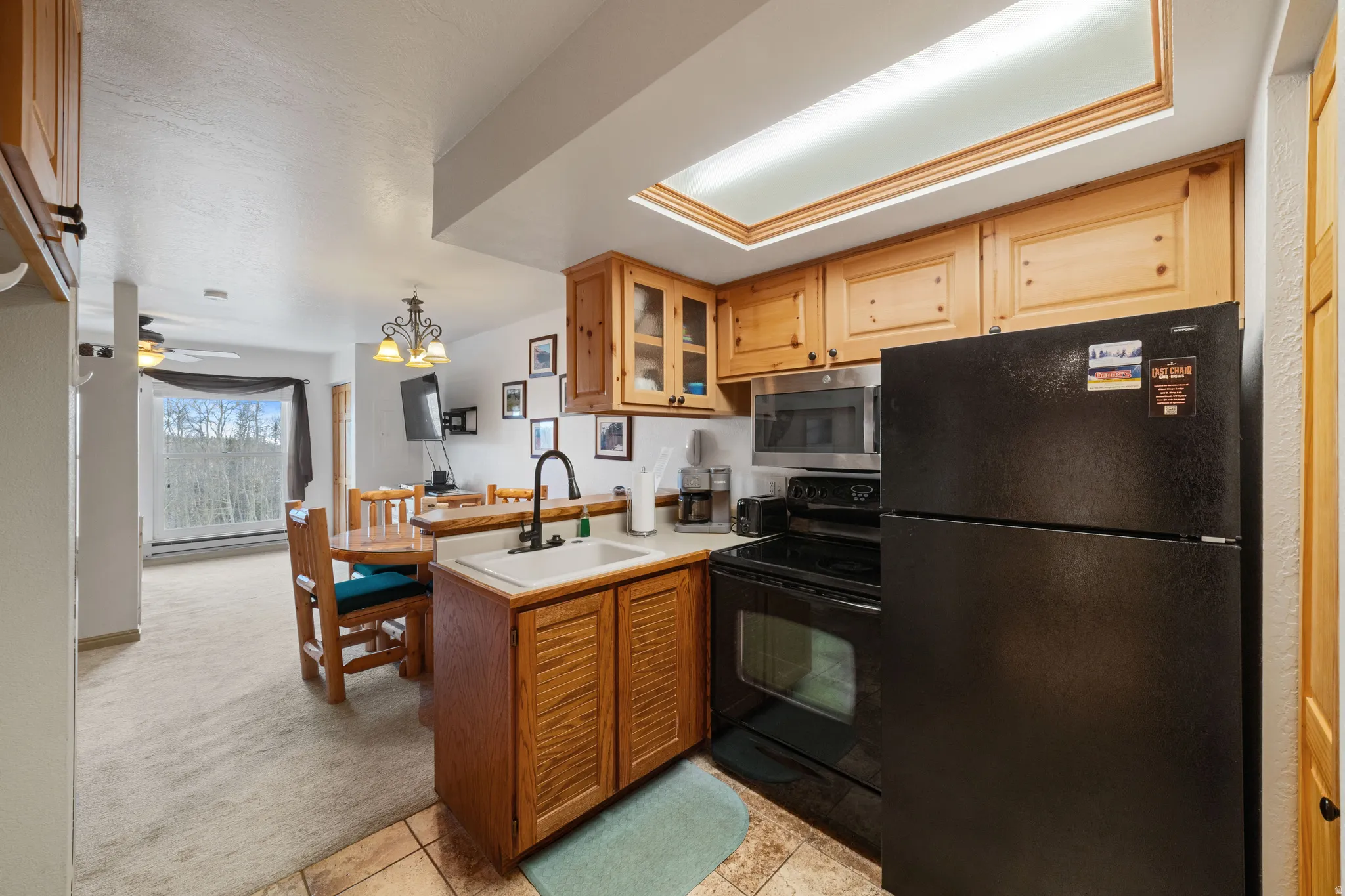 Kitchen with black appliances, light countertops, light colored carpet, glass insert cabinets, and hanging lights