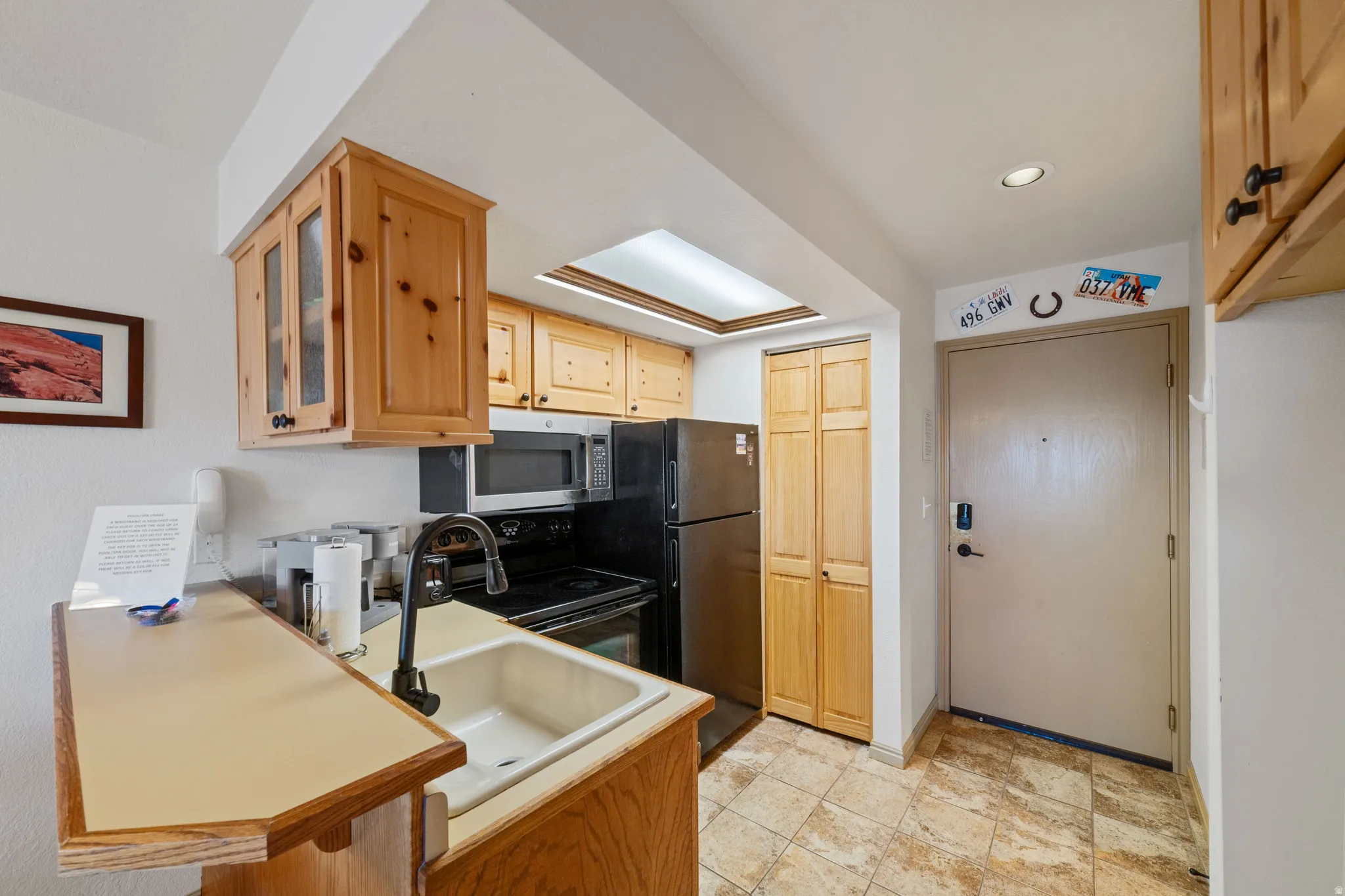 Kitchen featuring range with electric cooktop, light wood finish cabinetry, stainless steel microwave, light countertops, and glass fronted cabinets