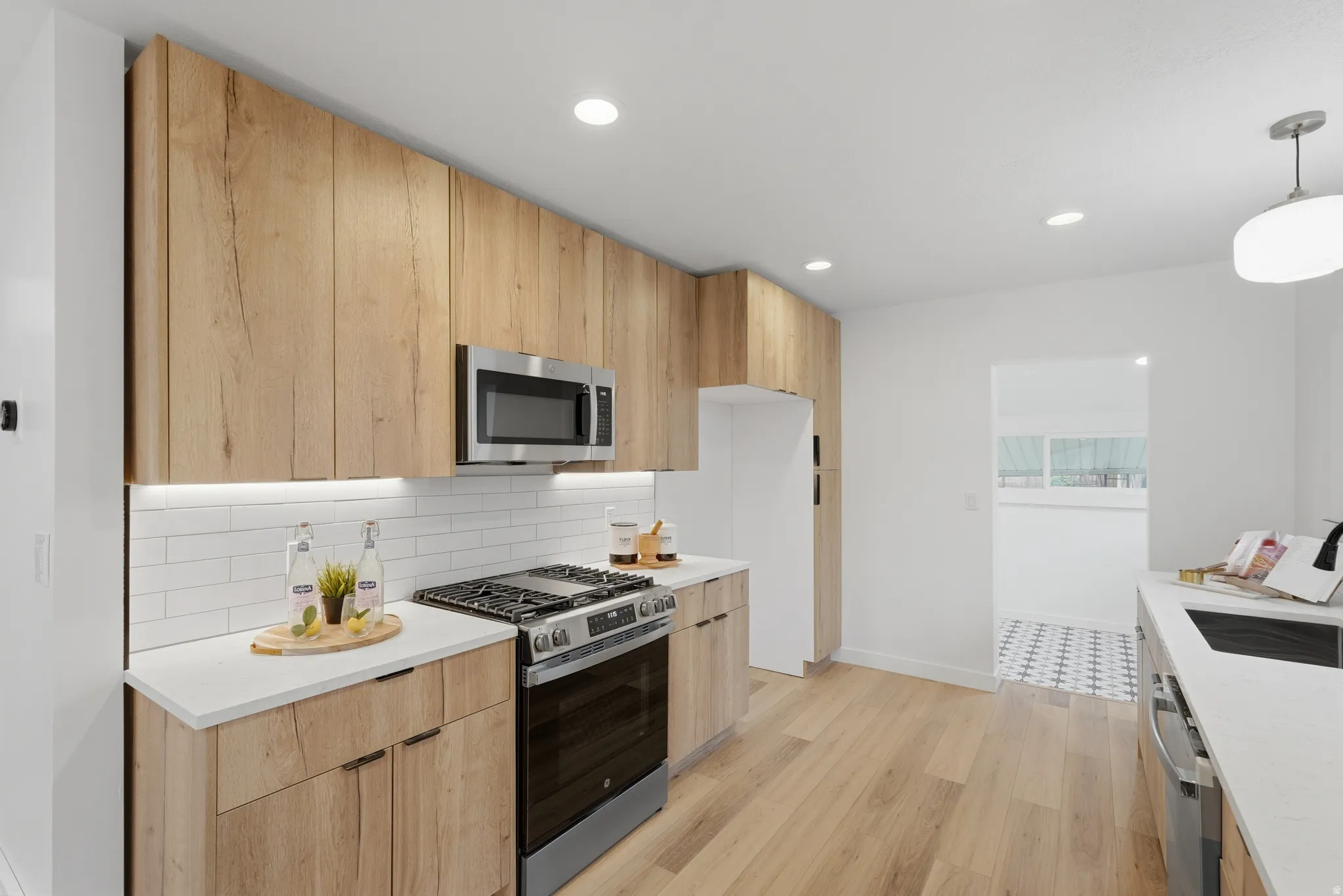 Kitchen featuring stainless steel appliances, modern cabinets, light stone countertops, light wood-style floors, and tasteful backsplash