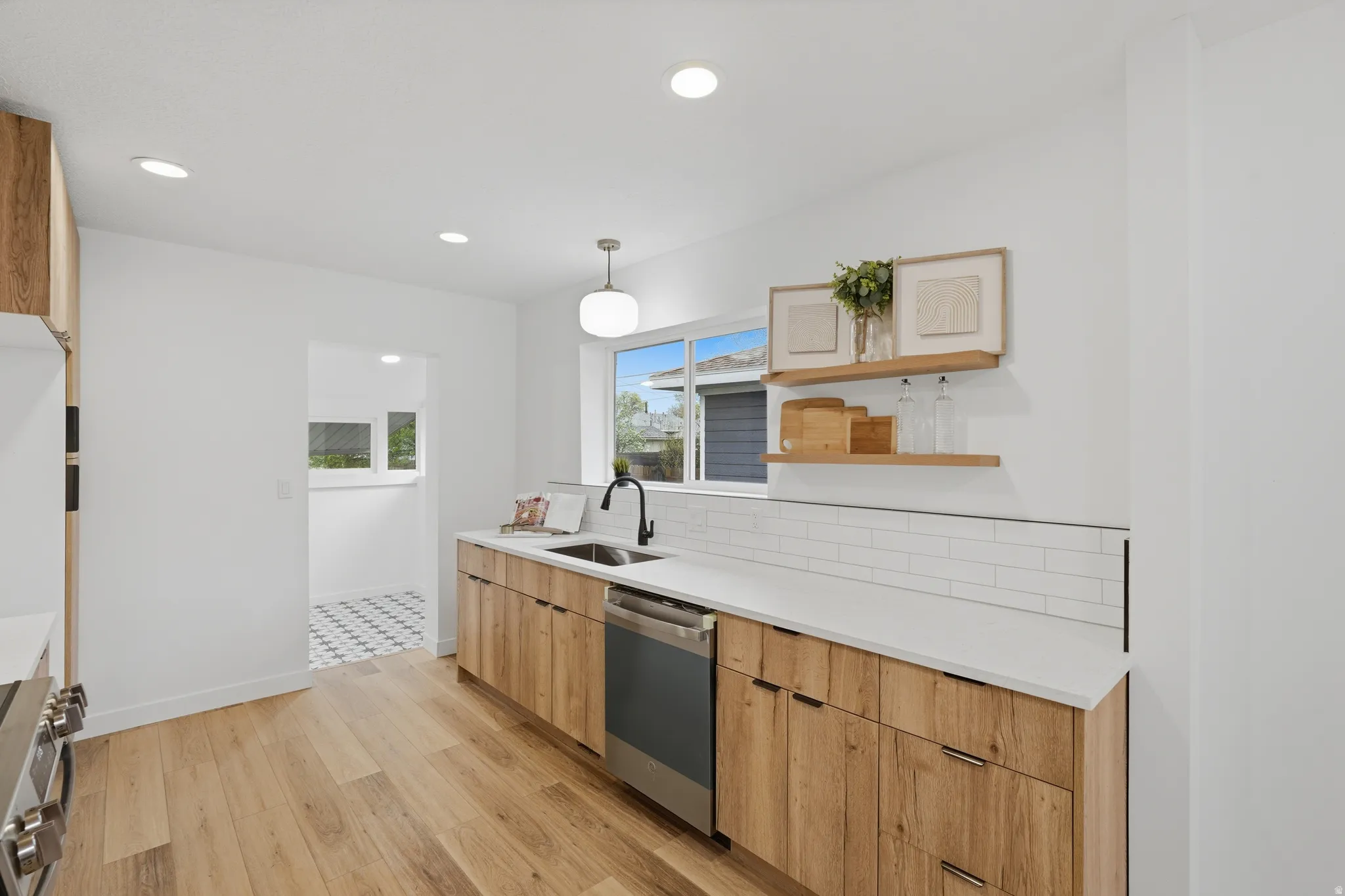 Kitchen with open shelves, light wood finish cabinetry, stainless steel appliances, light stone counters, and decorative light fixtures