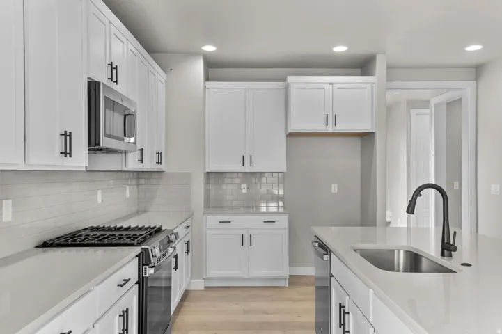 Kitchen featuring stainless steel appliances, light wood-style floors, white cabinetry, light stone countertops, and recessed lighting