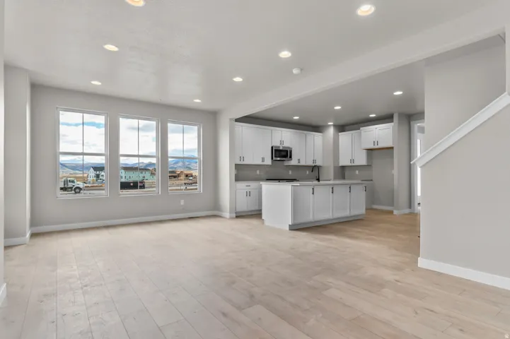 Kitchen featuring white cabinets, an island with sink, light countertops, open floor plan, and light wood finished floors