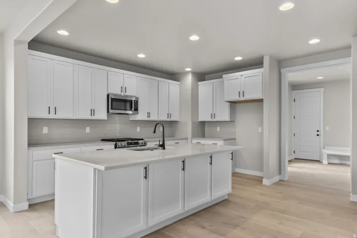 Kitchen featuring white cabinets, stainless steel appliances, an island with sink, backsplash, and light wood-style floors