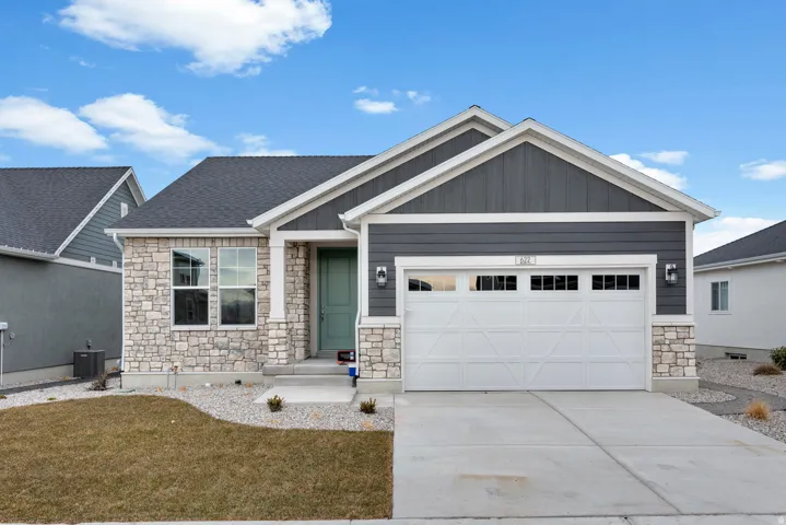 View of front of home with stone siding, board and batten siding, an attached garage, driveway, and a front lawn