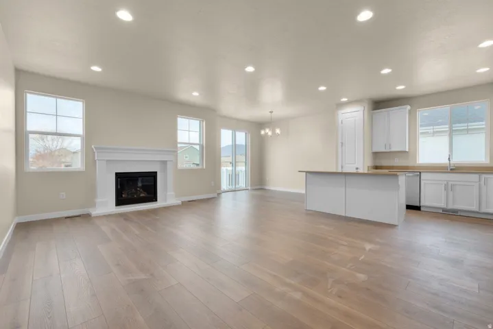 Unfurnished living room featuring light wood-style flooring, a glass covered fireplace, and hanging lights