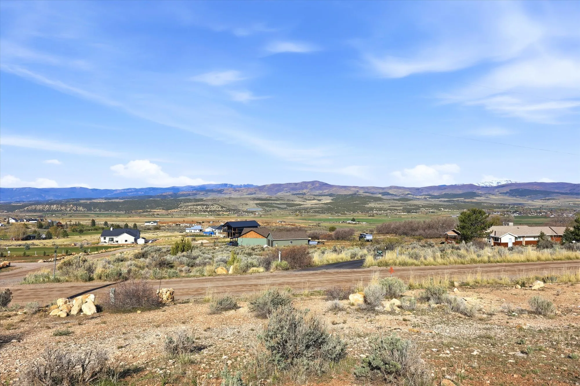 Expansive landscape featuring distant mountains with snow-capped peaks, rolling hills, and scattered residential properties