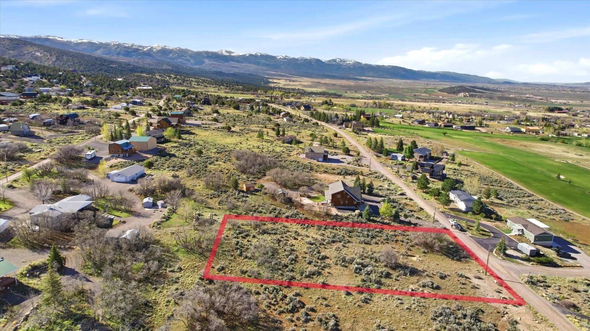 Expansive land parcel featuring natural shrubbery and partially paved road frontage