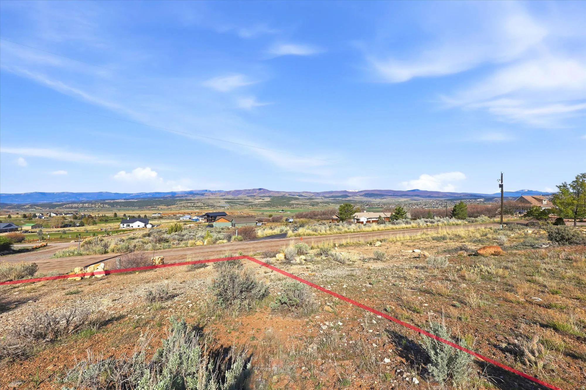 Expansive undeveloped land parcel featuring natural shrubbery and distant residential structures