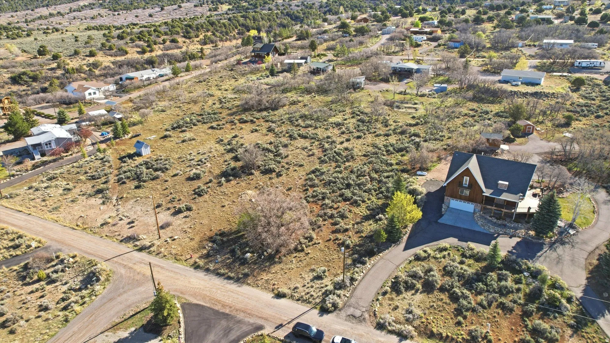 Expansive natural landscape surrounding a gabled roof residence featuring a stone-clad base, covered porch, and a paved driveway