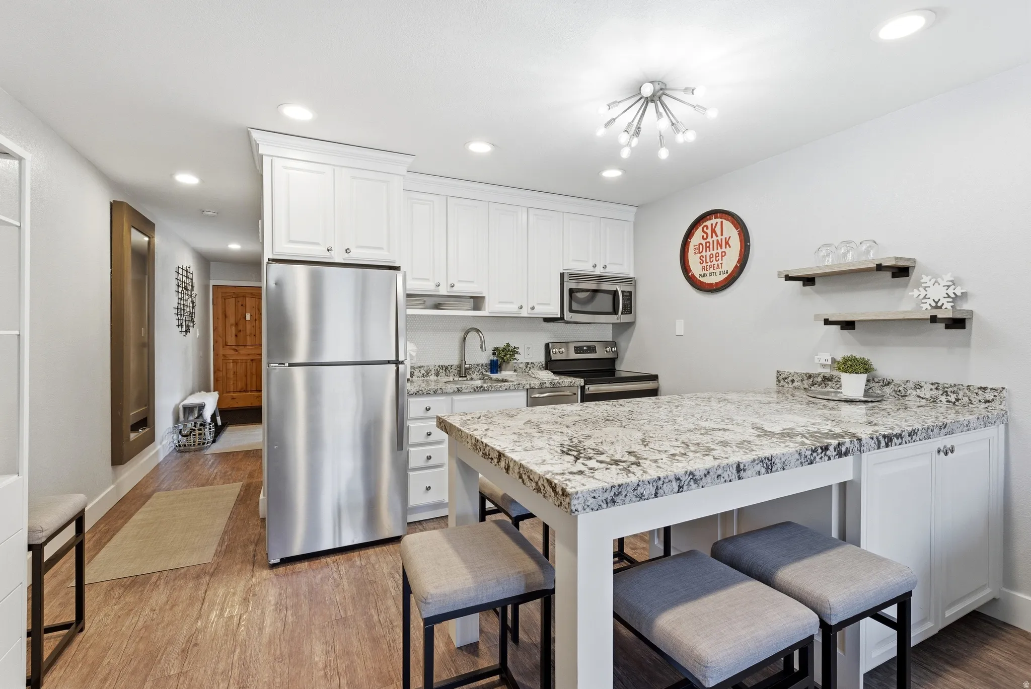 Kitchen with stainless steel appliances, a peninsula, white cabinetry, recessed lighting, and light wood finished floors