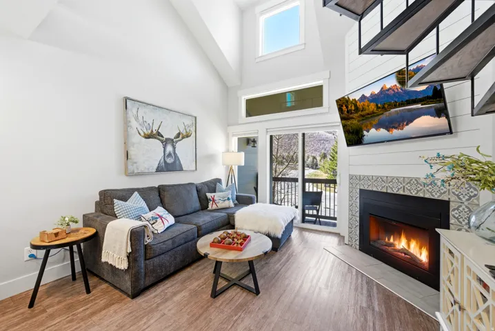 Living room with a high ceiling, light wood-style flooring, and a tiled fireplace