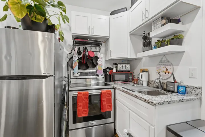 Kitchen featuring stainless steel appliances, white cabinetry, light stone counters, and open shelves