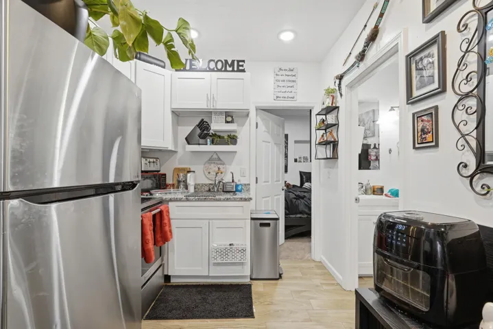 Kitchen with stainless steel appliances, white cabinets, light wood-type flooring, open shelves, and light stone counters