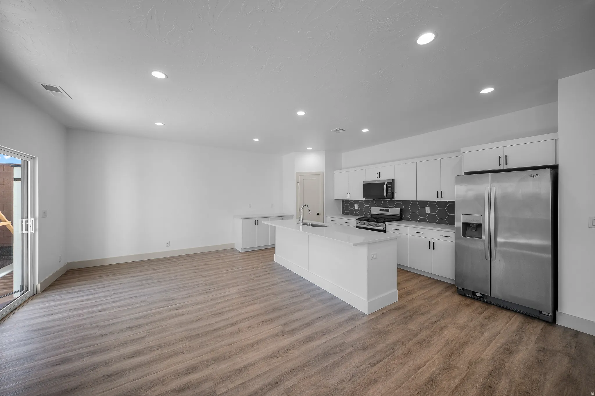 Kitchen with stainless steel appliances, white cabinetry, a kitchen island with sink, recessed lighting, and tasteful backsplash